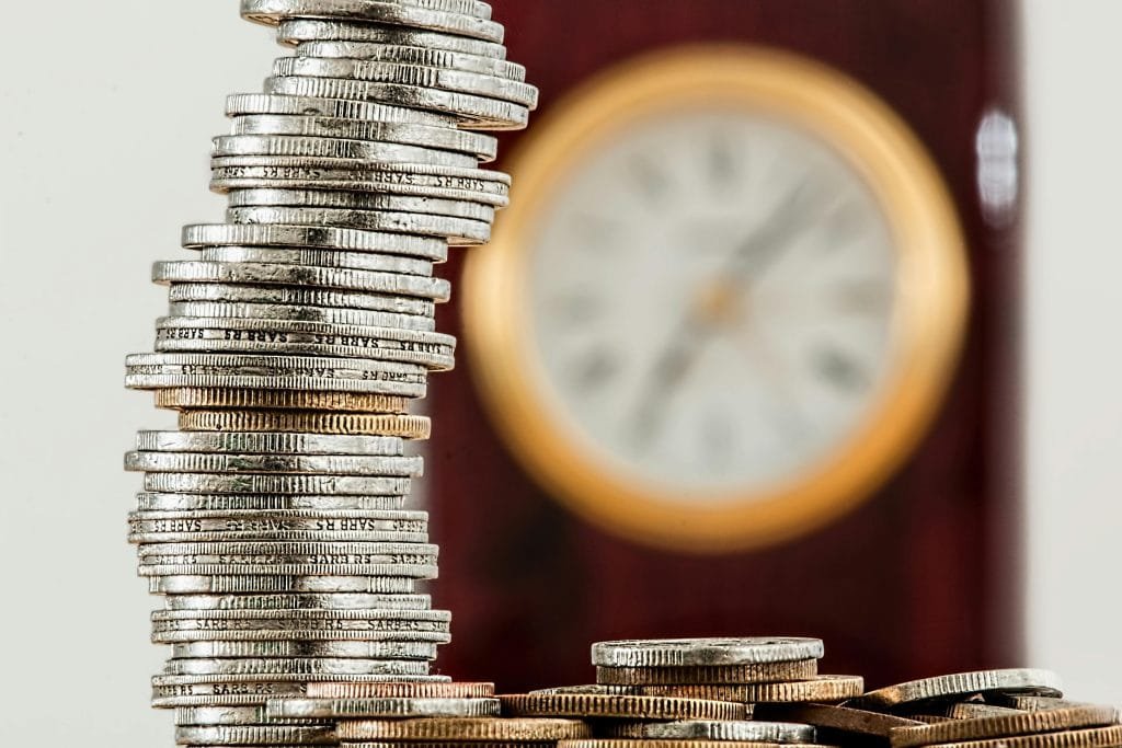 coins-currency-investment-insurance-128867-128867 - The Paystream A close-up image of stacked coins with a blurred clock, symbolizing time and money relationship.